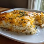 Ein St&uuml;ck cremiger H&auml;hnchen-Reis-Auflauf mit geschmolzenem K&auml;se und Petersilie auf einem wei&szlig;en Teller.