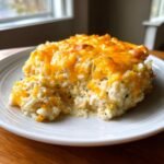 Ein cremiger H&auml;hnchen-Reis-Auflauf mit geschmolzenem Cheddar-K&auml;se auf einem wei&szlig;en Teller.