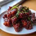 Nahaufnahme von Crispy Sweet Spicy Korean Chicken, glasiert und mit Sesam und Fr&uuml;hlingszwiebeln garniert.
