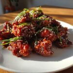 Ein Teller mit Crispy Sweet Spicy Korean Chicken, glasiert und bestreut mit Sesam und Fr&uuml;hlingszwiebeln.