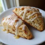 Zwei dreieckige Delicious Apple Scones With Maple Glaze mit Ahornsirup-Glasur auf einem wei&szlig;en Teller.