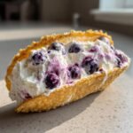 Nahaufnahme einer knusprigen Taco-Schale gef&uuml;llt mit cremiger Masse und Blaubeeren, perfekt f&uuml;r Delicious Blueberry Cheesecake Taco Shells.