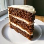 Nahaufnahme eines saftigen St&uuml;cks Delicious Gingerbread Cake mit drei Schichten dunklem Kuchen und wei&szlig;er Frischk&auml;se-Creme.