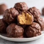 Nahaufnahme von Easy 4 Ingredient Peanut Butter Balls, einer ist angeschnitten und zeigt die cremige Erdnussf&uuml;llung.
