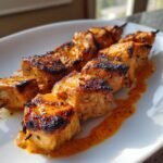 Nahaufnahme von gegrillten Easy Bang Bang Chicken Skewers mit w&uuml;rziger, oranger So&szlig;e auf einem wei&szlig;en Teller.