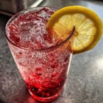 Nahaufnahme einer prickelnden, roten Erfrischende Italienische Soda mit Eisw&uuml;rfeln und einer Zitronenscheibe.