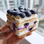 Nahaufnahme eines St&uuml;cks Refreshing Lemon Blueberry Icebox Cake, belegt mit frischen Blaubeeren und Puderzucker.
