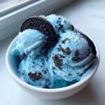 Nahaufnahme von drei Kugeln blauem Fun Cookie Monster Ice Cream mit dunklen Keksst&uuml;cken und einem ganzen Keks als Garnitur.