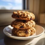 Drei gestapelte Healthy Oatmeal Cookies mit Rosinen auf einem wei&szlig;en Teller im Gegenlicht.
