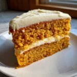 Nahaufnahme eines saftigen St&uuml;cks Irresistible Pumpkin Spice Cake mit dicker Schicht Frischk&auml;sefrosting.