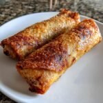 Nahaufnahme von zwei perfekt frittierten, knusprigen hausgemachten Egg Rolls auf einem wei&szlig;en Teller.
