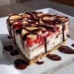 Ein reichhaltiges St&uuml;ck No Bake Banana Split Cheesecake mit Bananenscheiben, Erdbeersauce und viel dunkler Schokosauce.