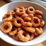 Nahaufnahme von Quick Delicious Hot Buttered Cinnamon Cheerios in einer wei&szlig;en Sch&uuml;ssel, gl&auml;nzend und zimtbestreut.