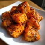 Nahaufnahme von glasierten Quick Easy Air Fryer Salmon Bites mit Kr&auml;utern auf einem wei&szlig;en Teller.