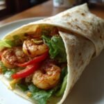 Nahaufnahme eines fertig gef&uuml;llten Quick Easy Shrimp Wrap mit Garnelen, Salat und Paprika auf einem wei&szlig;en Teller.