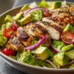 Geschnittenes gegrilltes H&auml;hnchen auf einem Quick Grilled Chicken Avocado Salad mit Avocado und roten Zwiebeln.