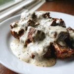 Nahaufnahme von zartem Schmorbraten, &uuml;bergossen mit cremiger Blauschimmelso&szlig;e mit Kr&auml;utern.