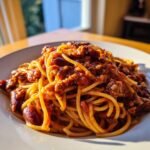 Nahaufnahme von Cowboy Spaghetti mit einer reichhaltigen, fleischigen So&szlig;e und roten Bohnen auf einem wei&szlig;en Teller.