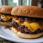 Nahaufnahme von zwei unwiderstehlichen Chopped Cheeseburgern mit geschmolzenem K&auml;se und karamellisierten Zwiebeln auf einem Teller.