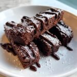 Nahaufnahme von gestapelten Chocolate Fruffles Brownie Fries, best&auml;ubt mit Puderzucker und betr&auml;ufelt mit dunkler Schokoladensauce.