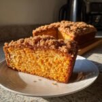 Ein St&uuml;ck saftiger Cozy Sourdough Pumpkin Coffee Cake mit goldbrauner Streuseldecke auf einem wei&szlig;en Teller.