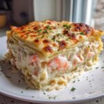 Nahaufnahme eines St&uuml;cks Cremige Seafood Lasagna mit &uuml;ppiger wei&szlig;er So&szlig;e, Garnelen und &uuml;berbackenem K&auml;se.