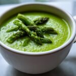 Nahaufnahme einer leuchtend gr&uuml;nen Cremige Spargelsuppe, garniert mit Spargelspitzen in einem wei&szlig;en Becher.