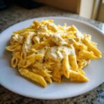 Nahaufnahme von cremiger White Cheddar H&auml;hnchen-Pasta mit Penne-Nudeln auf einem wei&szlig;en Teller.