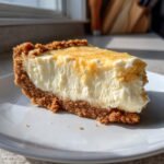 Ein cremiges St&uuml;ck Cheesecake Pie mit goldbraunem Keksboden, beleuchtet von Sonnenlicht.
