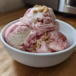 Drei Kugeln cremiges Erdbeer-Cheesecake Eis mit Keksstreuseln in einer wei&szlig;en Schale.