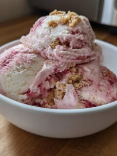 Drei Kugeln cremiges Erdbeer-Cheesecake Eis mit Keksstreuseln in einer weißen Schale.