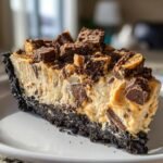 Nahaufnahme eines cremigen St&uuml;cks Decadent Butterfinger Pie mit dunklem Keksboden und Butterfinger-St&uuml;cken obenauf.