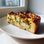 Ein dickes St&uuml;ck Delicious Artichoke Broad Bean Tart mit goldbrauner, gebackener Kruste auf einem wei&szlig;en Teller.