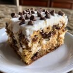 Ein St&uuml;ck Delicious Chocolate Peanut Butter Poke Cake mit wei&szlig;em Frosting und Schokotropfen.