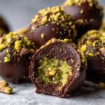 Nahaufnahme von Delicious Dubai Chocolate Balls, einer aufgeschnitten, die gr&uuml;ne Pistazienf&uuml;llung zeigt.