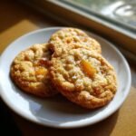 Drei Delicious Peach Cobbler Cookies mit Zuckerkristallen und Pfirsichst&uuml;cken auf einem kleinen wei&szlig;en Teller.