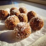 Mehrere selbstgemachte Easy Energy Balls, bestreut mit Kokosflocken, liegen auf einem St&uuml;ck Backpapier.