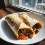 Zwei saftige Easy Philly Cheesesteak Roll Ups gef&uuml;llt mit Rindfleisch und Paprika auf einem wei&szlig;en Teller.