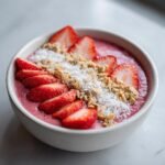 Nahaufnahme einer k&ouml;stlichen Erdbeer Smoothie Bowl mit frischen Erdbeerscheiben, Kokosraspeln und N&uuml;ssen.
