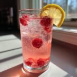 Nahaufnahme eines kohlens&auml;urehaltigen Getr&auml;nks mit Himbeeren und einer Zitronenscheibe: Erfrischende Himbeer-Limonade.