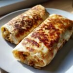 Zwei goldbraun gebratene Flavorful Cajun Black Bean Chicken Burritos auf einem hellen Teller.