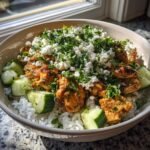 Nahaufnahme einer Sch&uuml;ssel mit Griechische Chicken Bowls With Cucumber Salad: Reis, gew&uuml;rztes H&auml;hnchen, Gurkenst&uuml;cke, Feta und Petersilie.