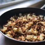 Nahaufnahme eines Ground Turkey And Cauliflower Skillet mit gebratenem Hackfleisch und Blumenkohlr&ouml;schen in einer schwarzen Pfanne.