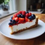 Ein St&uuml;ck cremiger Heavenly Berry Cheesecake mit einem Keksboden, belegt mit Erdbeeren, Himbeeren und Blaubeeren.