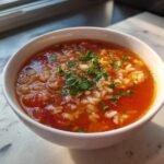 Nahaufnahme einer herzhaften Tomaten-Reis-Suppe mit Reis und Petersilie in einer wei&szlig;en Sch&uuml;ssel.