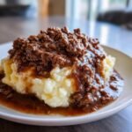 Nahaufnahme von herzhaftem Rinderhackfleisch mit So&szlig;e &uuml;ber cremigem Kartoffelp&uuml;ree auf einem wei&szlig;en Teller.