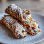Drei frisch gef&uuml;llte Italienische Cannoli, best&auml;ubt mit Puderzucker, auf einem wei&szlig;en Teller.