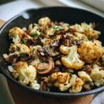 Nahaufnahme eines Knoblauch Blumenkohl Pilz Pfannengericht mit gebratenem Blumenkohl und Pilzen in einer gusseisernen Pfanne.