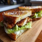 Nahaufnahme eines halbierten, knusprigen Chicken Caesar Sandwich mit goldbraunem Toastbrot und viel Salat.