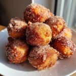 Ein Haufen goldbrauner, frittierter Teigb&auml;llchen, bedeckt mit glitzerndem Zimt-Zucker, die k&ouml;stliche Zimt-Zucker-Donut-L&ouml;cher darstellen.